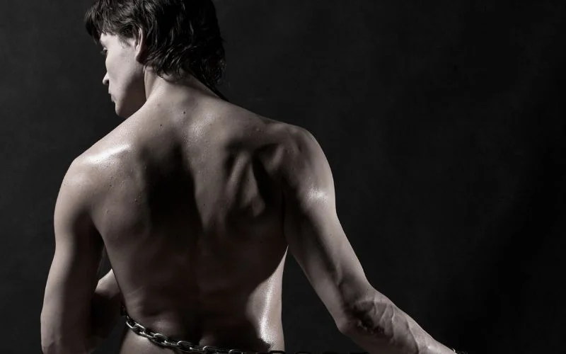 Back-view male nude portrait emphasizing body contours and shadows