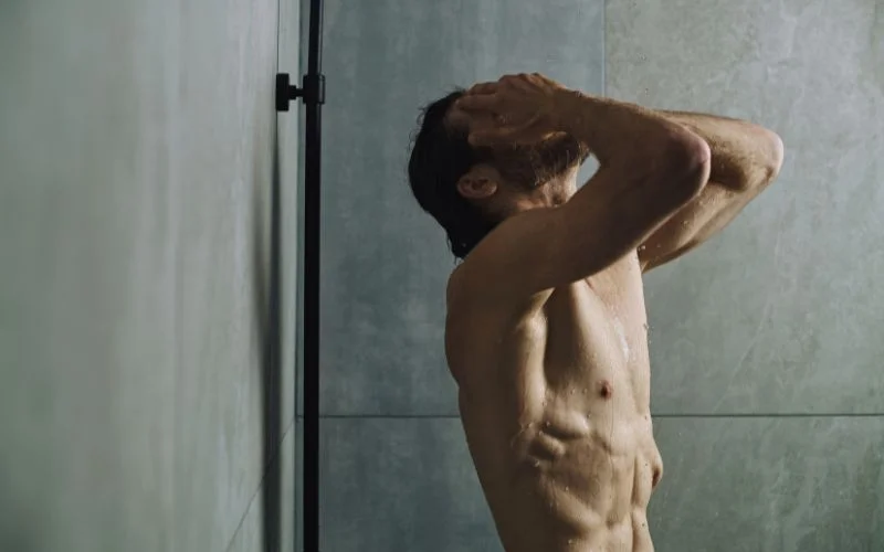 Male nude shower pose with water droplets and moody lighting