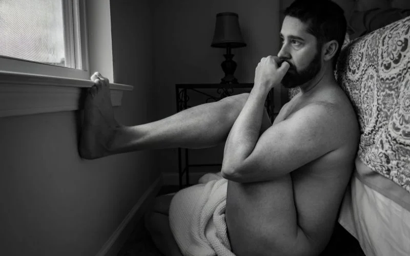 Side-profile male nude photography pose with soft studio lighting
