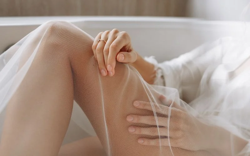 Aesthetic nude bridal photos showing a bride wrapped in sheer white fabric on a bed