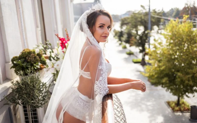 Nude wedding photoshoot of a bride in lace lingerie and a veil standing in a garden setting