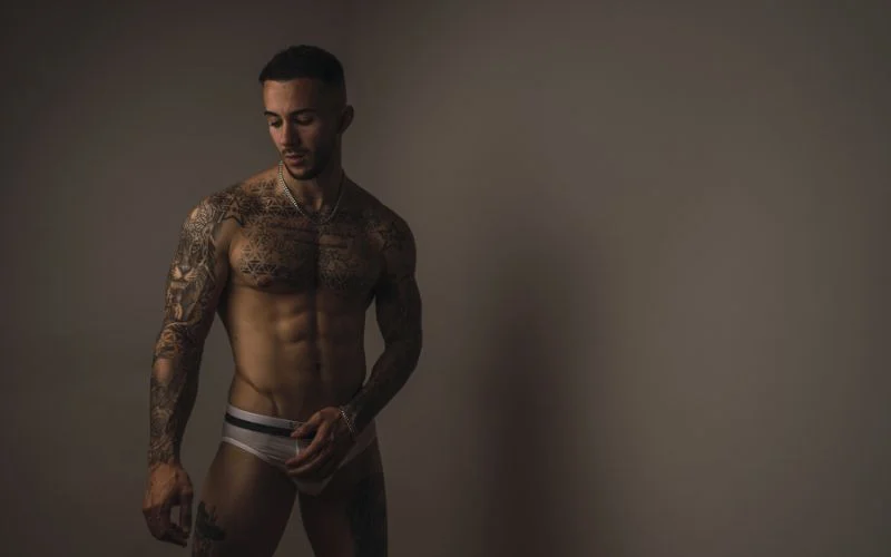 Confident model flexing muscles in a bold masculine boudoir pose with moody lighting