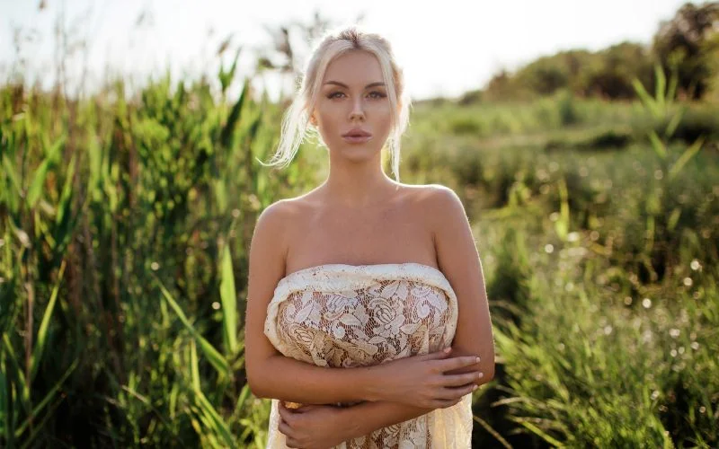 Nude wedding photography of a bride standing in a tall grass field wrapped in sheer fabric