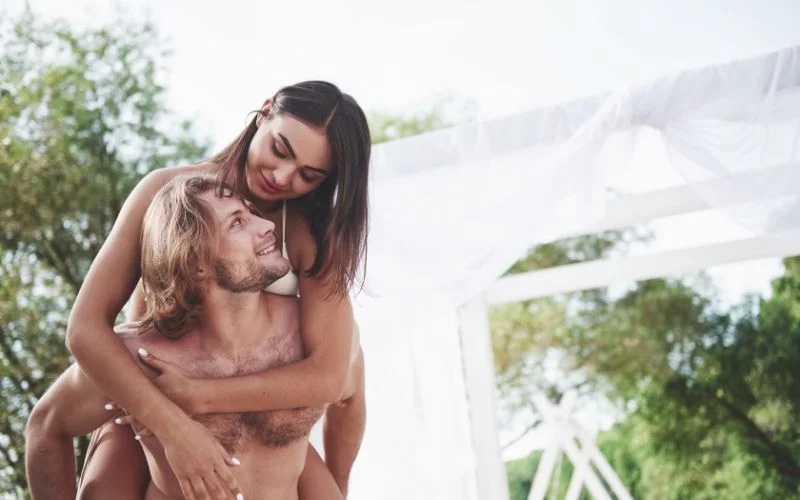 Nude wedding images of a couple embracing outdoors near a white draped structure