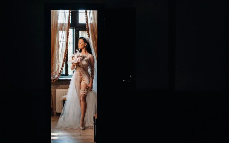 Simple bridal nude photography of a bride standing in a doorway lit by natural light