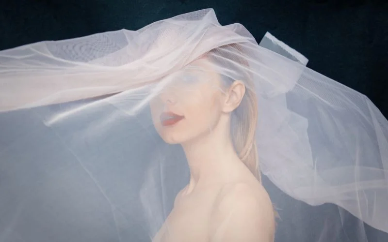 Wedding boudoir nude portrait of a bride draped in a sheer veil against a dark backdrop