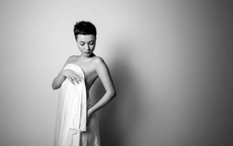 Black and white nude wedding photography of a bride wrapped in fabric against a plain backdrop