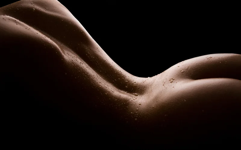 Gentle back arch pose in nude plus size photography, emphasizing curve and light play along the spine