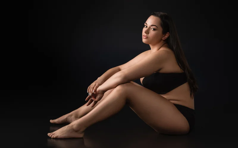 Side profile nude plus size boudoir shot capturing the natural curve of the back and hip in soft light