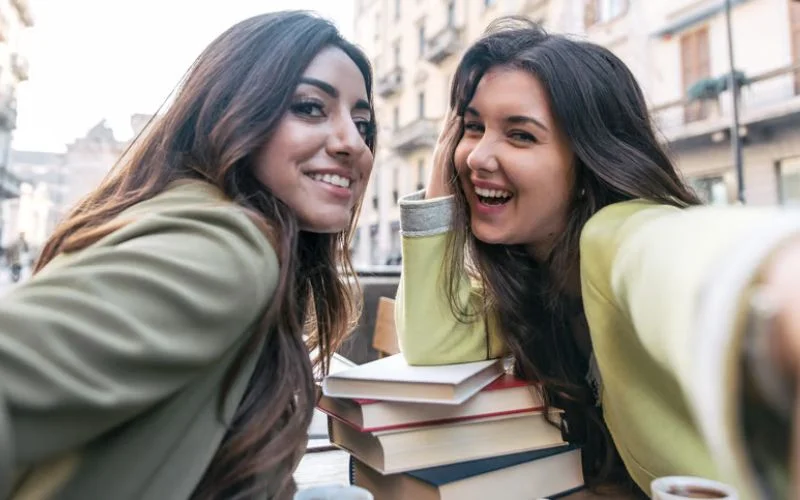 Two friends sitting side by side reading books together