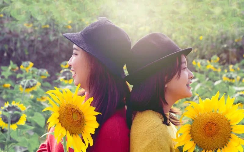Candid best friend poses for 2 females holding sunflowers in an outdoor field