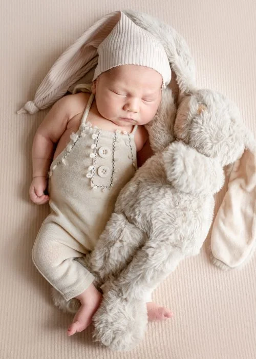 Newborn photoshoot poses with baby lying in a cream knit outfit beside a soft toy