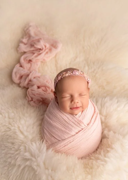 Newborn poses for beginners with baby swaddled in pink and wearing a floral headband