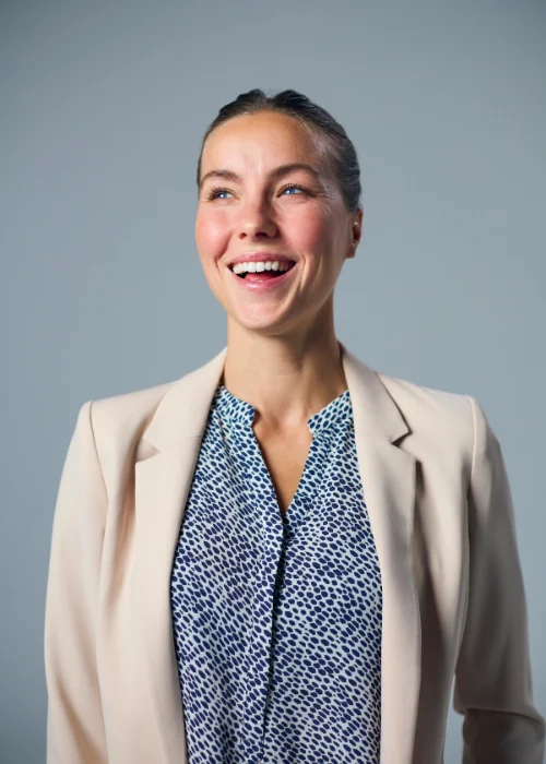 Professional corporate headshot with a natural smile in a relaxed sideways pose.