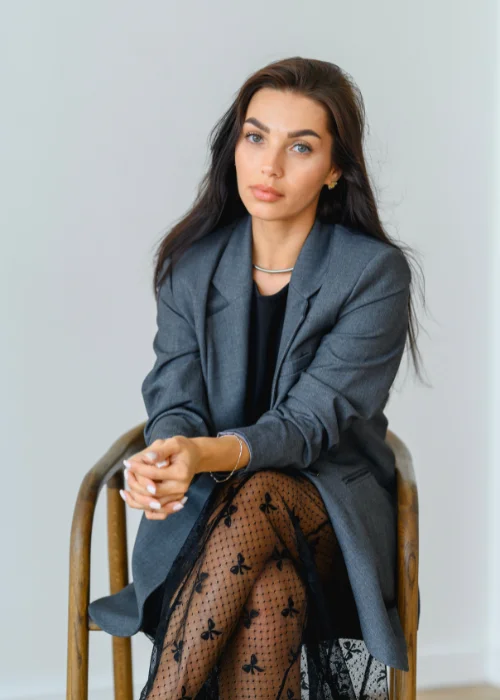 Professional headshot featuring an elegant crossed leg pose and confident posture.