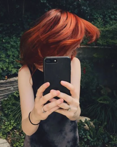 Person partially covering their face with a hat, book, or phone for a creative and mysterious selfie composition.