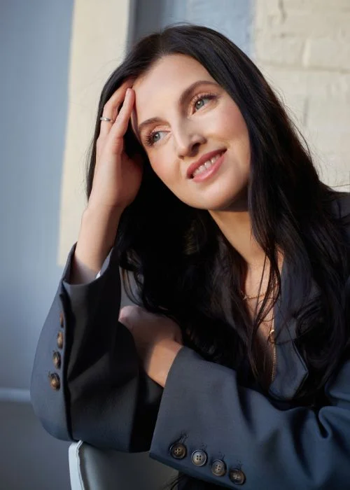 Professional woman resting her hand on her forehead in a relaxed headshot pose.