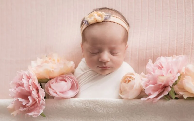 Sleeping newborn in a blush pink monochrome setup surrounded by pink peonies