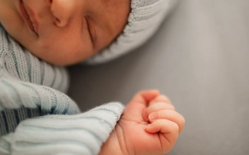 Close-up of a newborn's tiny hand and face against a cream knit sweater