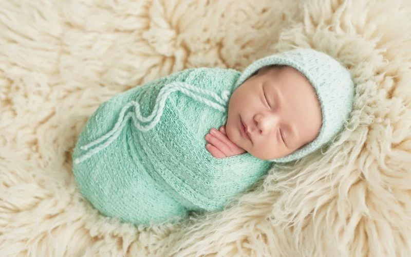 Newborn potato sack pose with baby curled in a mint green knit wrap and matching hat