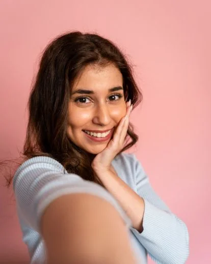 Person framing their face with both hands while capturing a creative and expressive selfie portrait.