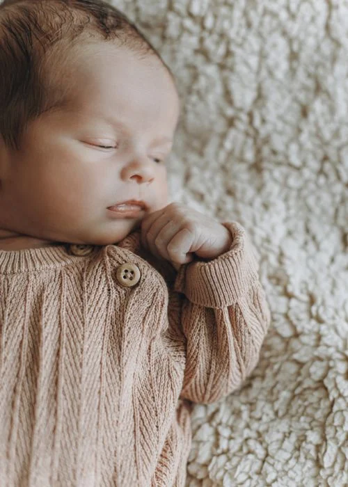 Newborn curled up sleeping on a soft beige fabric backdrop, side profile view