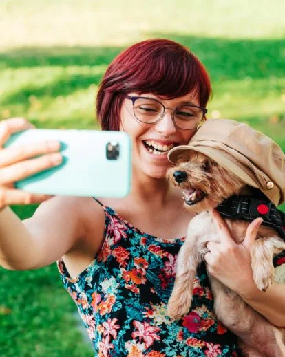 Smiling person taking a selfie while cuddling their dog, creating a warm and natural selfie pose idea.