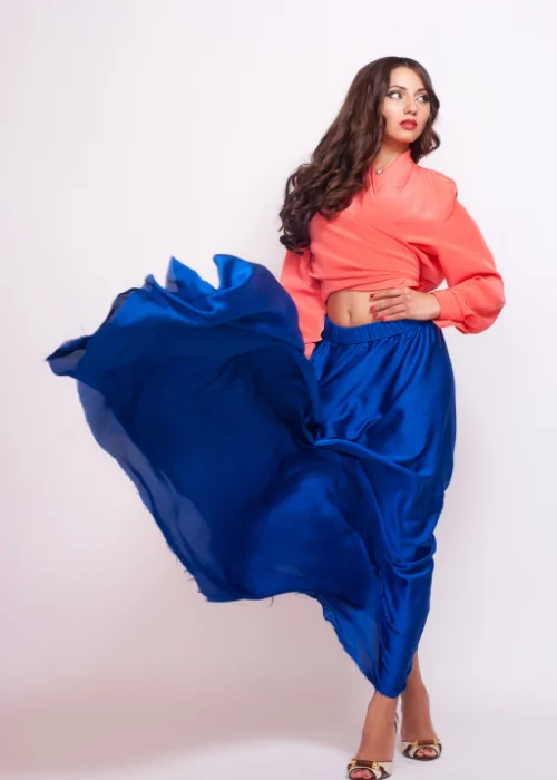 Woman in a coral top and flowing blue skirt captured mid-movement in a studio setting