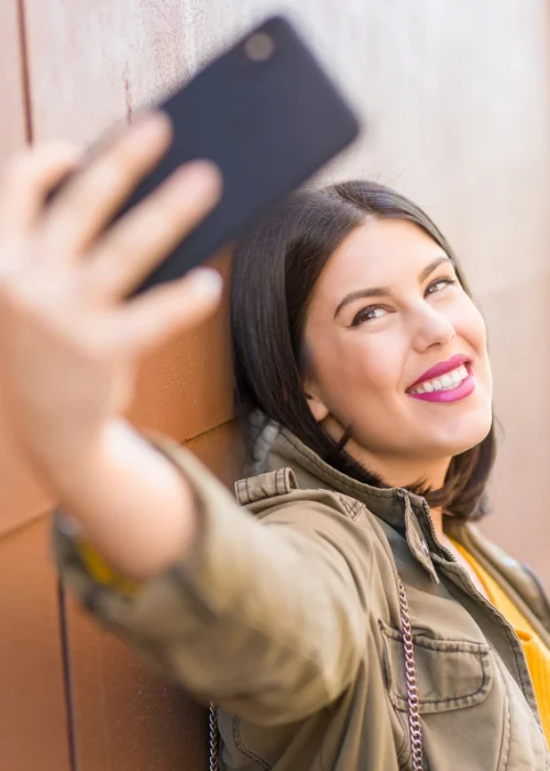 Full body self portrait of a woman taking a selfie against a wooden wall