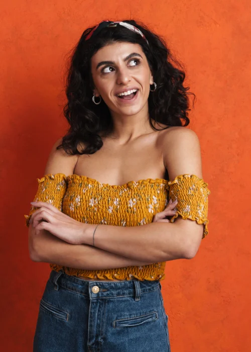 Upper body portrait of a woman in an orange top, arms crossed, against an orange backdrop