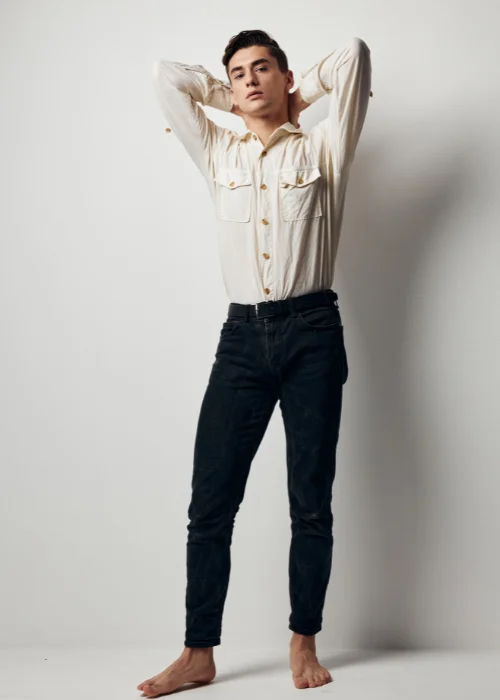 Man in a cream shirt and dark jeans posed with arms raised, demonstrating lens choice for full body portrait photography