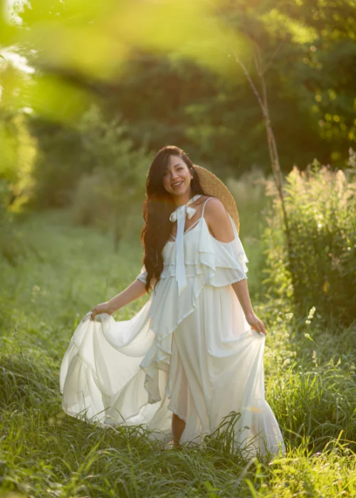 Woman in a flowing white dress walking through sunlit grass, fabric moving with her stride