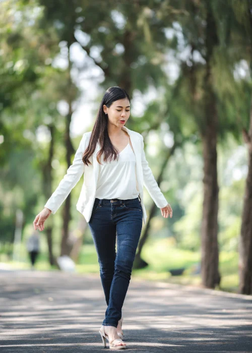 Woman walking candidly along a tree-lined path in a white top and jeans