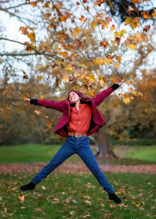 Woman jumping mid-air with arms outstretched among autumn leaves