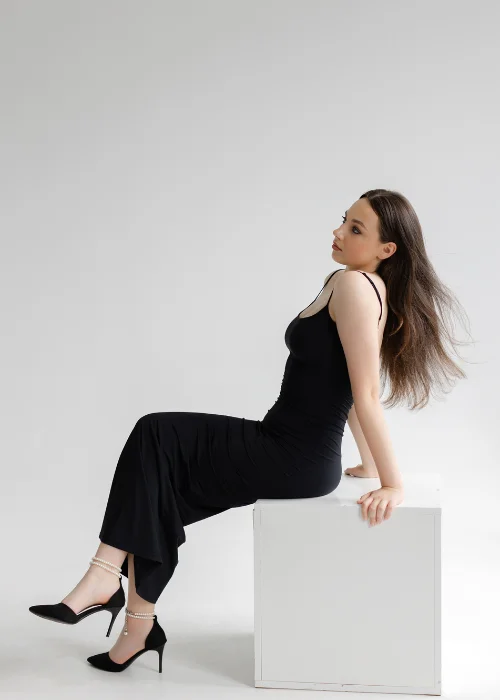 Whole body portrait of a woman sitting sideways on a white cube in a studio