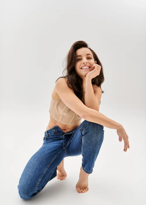 Woman kneeling on the floor in a tan top and jeans, resting her chin on her hand