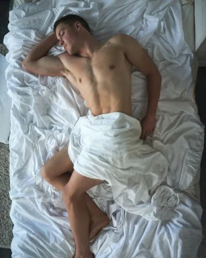 Male boudoir photography pose using bed sheets for artistic composition