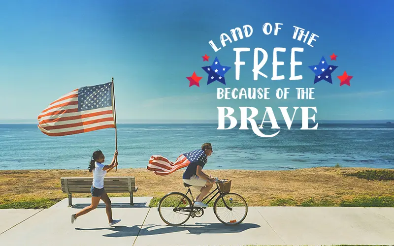 Memorial Day overlay reading "Land of the Free Because of the Brave" on beach photo with flag