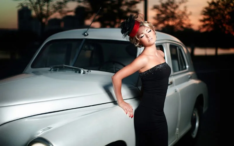 woman in a vintage black dress leaning against the hood of a classic car