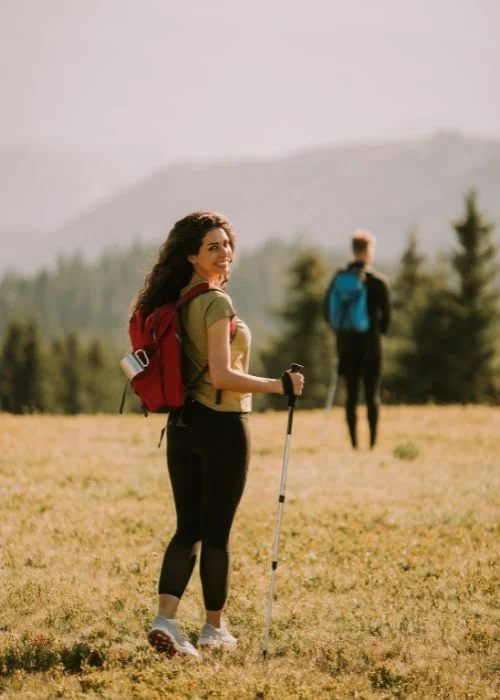 Female hiker looking back toward the camera while holding trekking poles in an open meadow, a great example of hiking picture poses.