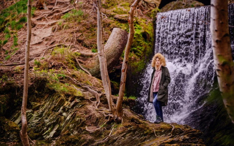 Hiker posing in front of a cascading waterfall, creating a striking hiking portrait with a natural backdrop.