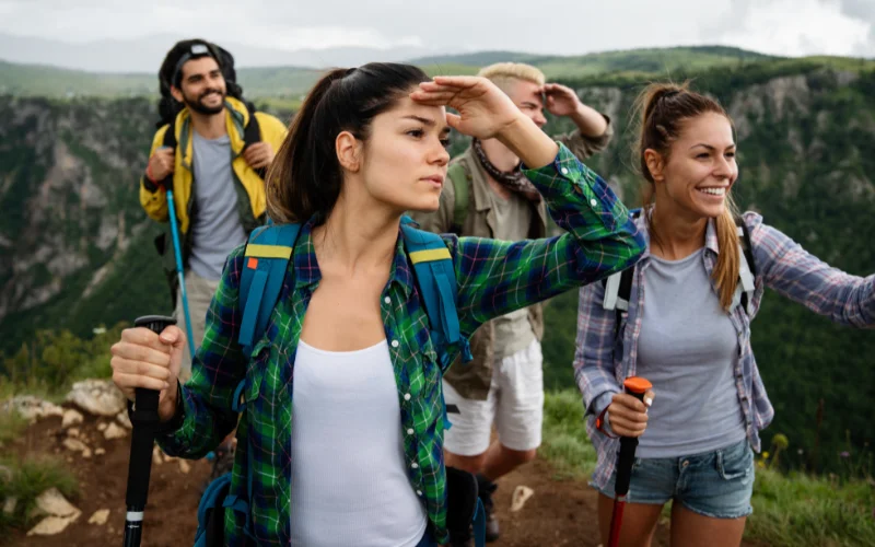Group of friends posing together on a hiking trail with mountains and forests in the background.