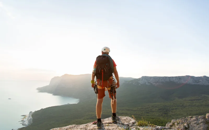 Hiker standing at a viewpoint and looking toward distant mountain peaks in a thoughtful hiking pose.