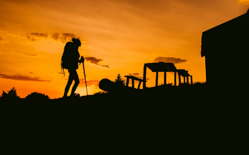 Silhouette of a hiker standing on a ridge at sunset, creating a dramatic hiking photography composition.