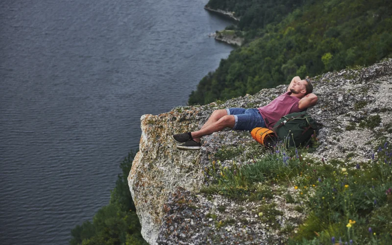 Hiker relaxing on a grassy hillside and enjoying the view during an outdoor adventure.