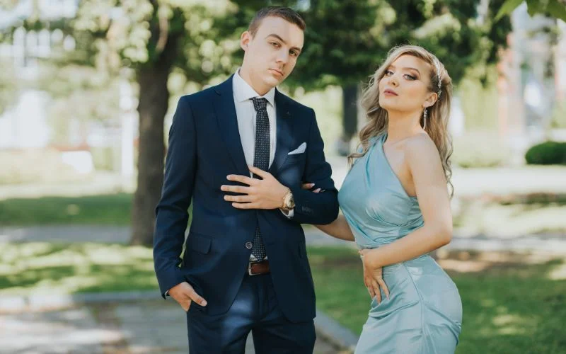 Prom couple poses of a couple standing arm in arm outdoors under trees