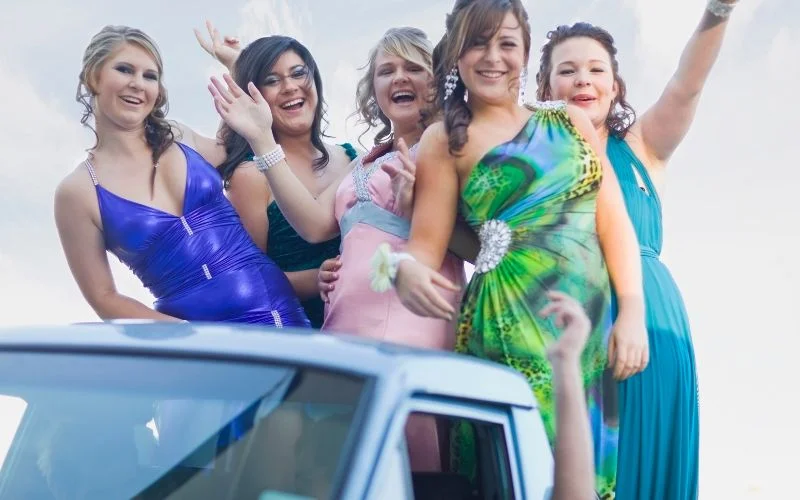 Fun prom poses with a group of friends leaning out of a car window smiling
