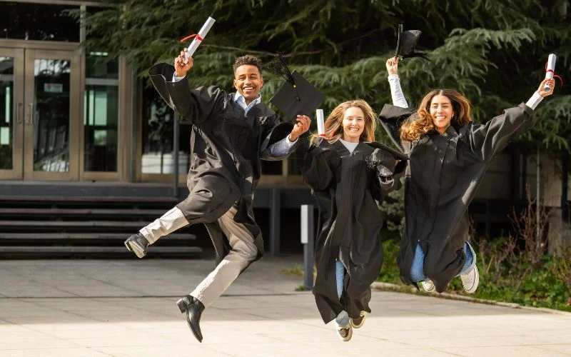 Grad pic poses of three graduates jumping in the air together with arms raised in celebration