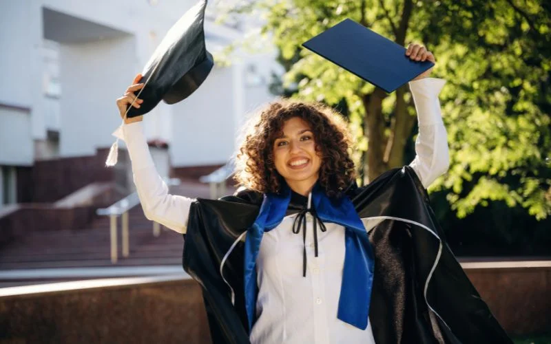 Graduation pose for guys with a graduate holding her cap up in one hand and diploma in the other