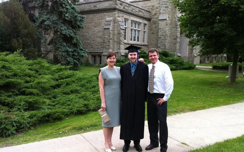 Graduation poses with family showing a graduate standing between two family members on campus